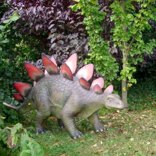 Eine Dinosaurierfigur steht vor einem Strauch