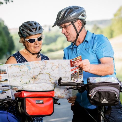 Ein Ehepaar begutachtet eine Landkarte während sie auf ihren Fahrrädern sitzen